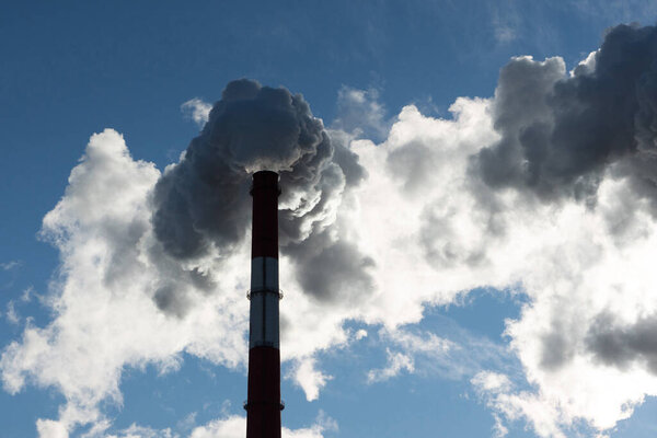 Smoking pipes of thermal power plant against blue sky. Large blue pipe releases white steam. Fuming chimneys of a factory polluting.