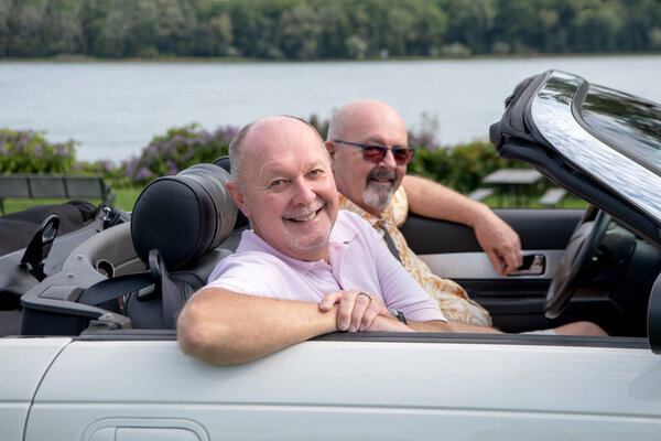 Older male LGBT gay couple enjoying  a sunny day and driving in their white convertible with the top down.  The couple is smiling and happy.