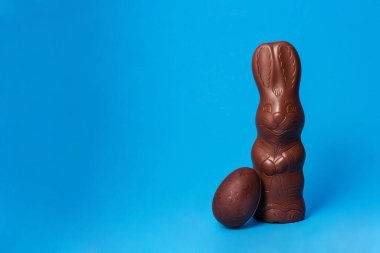 Paskalya Tavşanı ve Çikolatalı Yumurta Mavi Arkaplan Yaratıcı Paskalya Tatili Konsepti. jpg