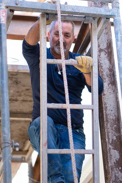  İnşaat işçisi duvarı onarmak için merdivene tırmandı..