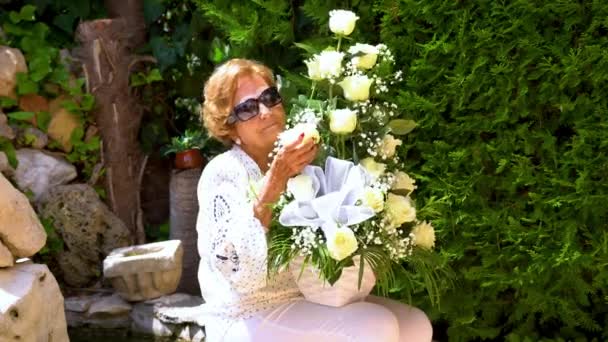 Spännande vacker äldre kvinna luktar vita rosor . — Stockvideo