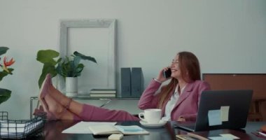 Mutlu, çekici patron iş kadını gülümsüyor cep telefonuyla konuşuyor ofis masasında bacakları var..