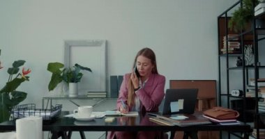 İş stresi. Güzel ciddi iş kadını telefonla konuşuyor, ofis masasında dizüstü bilgisayarla çalışıyor..