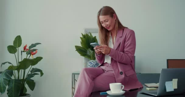 Social networks concept. Happy beautiful elegant business woman using smart phone mobile app at light office workplace. — Stock Video