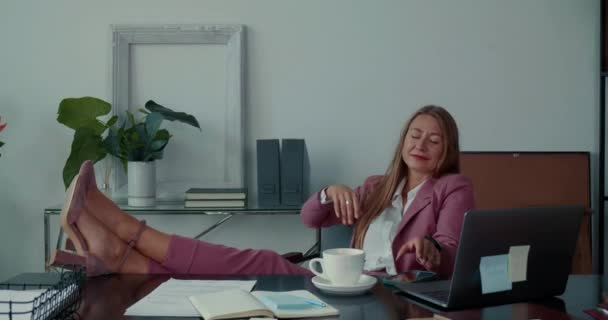 Sin estrés. Feliz hermosa mujer de negocios con piernas en la mesa de la oficina pone el teléfono inteligente para relajarse, descansar en el lugar de trabajo. — Vídeo de stock