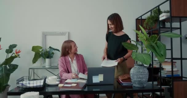 행복하고 젊은 두 젊은 전문직 여성 이 노트북 컴퓨터와 함께 현대 사무실 테이블에서 협력하는 일을 한다. — 비디오