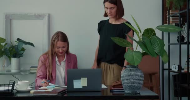 Coopération sur le lieu de travail. Deux belles jeunes femmes d'affaires professionnelles occupées parlent de travailler avec un ordinateur portable ensemble. — Video