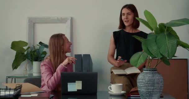 Trabajo en equipo y cooperación. Dos hermosas mujeres de negocios felices jóvenes utilizan el ordenador portátil juntos lluvia de ideas en la mesa de la oficina. — Vídeos de Stock