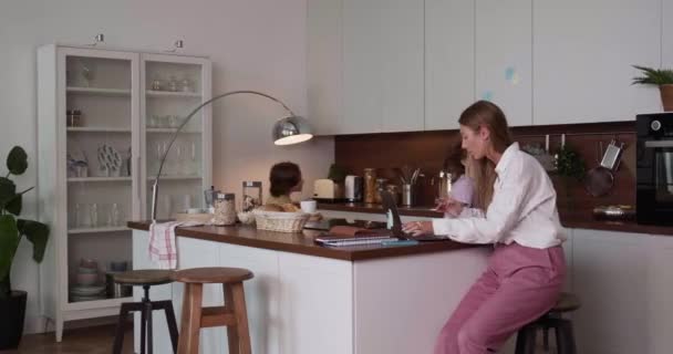 Beautiful business woman trying to work using laptop at spacious home kitchen table, noisy children run around shouting. — Stock Video