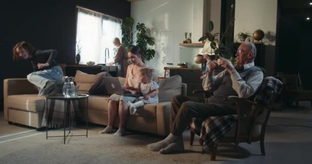 Brede shot gestresste mooie vrouw met behulp van laptop met baby meisje omringd door familieleden en lawaaierige kinderen in groot huis. — Stockvideo