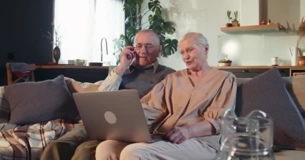 Feliz bela aposentado anos 70 caucasiano mulher homem de ensino para usar laptop no sofá na sala de estar luz. Conceito de comércio eletrónico — Vídeo de Stock