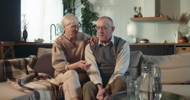 Conceito de integridade. Retrato de feliz aposentado anos 70 casal sênior, marido e esposa sorriso, conversa sentado no sofá em casa — Vídeo de Stock