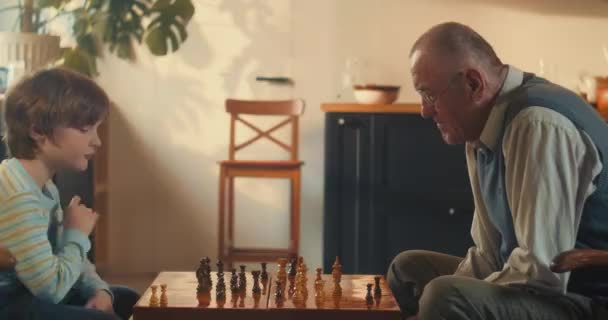 KLEINES GENIUS Nettes Teenie-Knabenkind beim Schachspielen gegen den Großvater der 70er Jahre. Entwicklung logischen Denkens. — Stockvideo