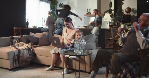 MULTI GENERATION FAMILY TOGETHER Duas crianças adolescentes correm ao redor feliz jovem mãe usando laptop com bebê. velho avô. — Vídeo de Stock