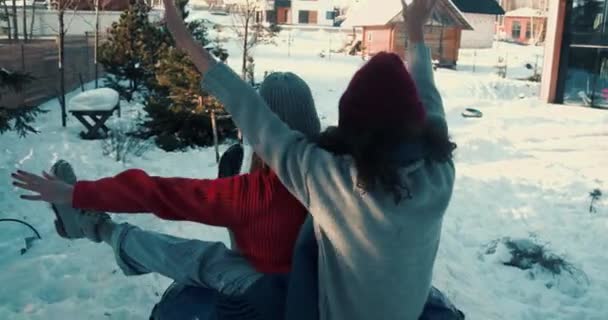 Камера следит за двумя счастливыми возбужденными красивыми 20-летними женщинами, катающимися на санках вместе на домашней террасе, наслаждаясь зимним весельем. — стоковое видео
