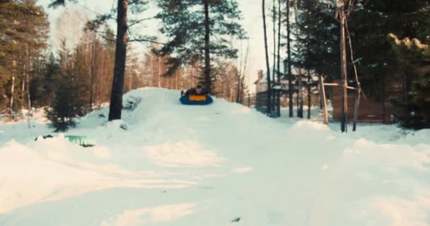 Зима веселье на снегу. Веселый 20-летний мужчина наслаждается катанием на санках на надувных санях в замедленной съемке солнечного леса. — стоковое видео