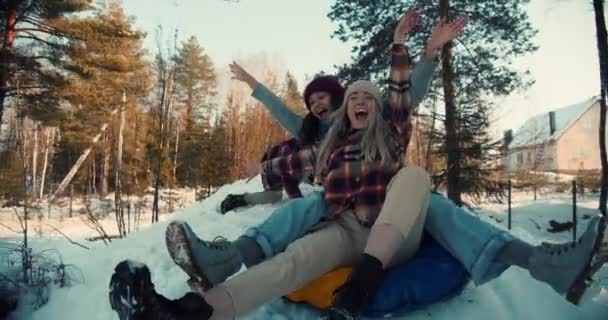 Zwei attraktive, multiethnisch glückliche Frauen lächeln beim Rodeln auf dem Schneehang in Richtung Kamera, Winterwochenende Spaß in Zeitlupe. — Stockvideo