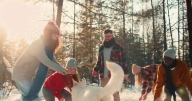 Birlikte Noel tatili. Mutlu çoklu etnik arkadaşlar ve köpekler karla oynayıp güneşli ormanda ağır çekimde oynuyorlar..