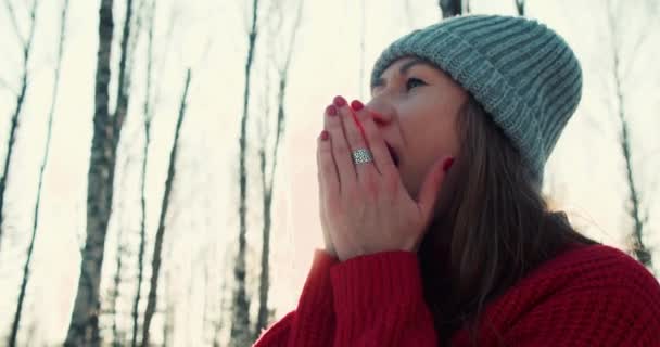 Happy beautiful young 30s woman in red sweter, hat warms hands with breath in sunny cold winter forest slow motion — Stok Video