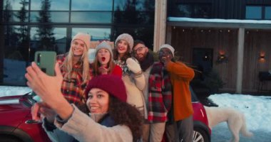 Noel tatili. Mutlu eğlenceli çoklu etnik arkadaşlar gülümser, kırmızı arabada selfie çekerler, karlı ev terasında ağır çekimde..