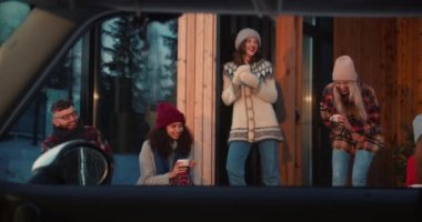 Açık araba penceresinden bakmak, bir grup mutlu arkadaş sohbeti, rahat ahşap kışlık terasta sıcak içeceklerin tadını çıkarmak ağır çekim.