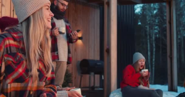 Świąteczne przyjęcie na zewnątrz. Szczęśliwy pozytywny przyjaciele pić herbatę, usiąść na torby fasoli w przytulnym zimowym tarasie domek slow motion. — Wideo stockowe
