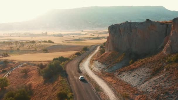 Drone camera volgt witte auto langs epische prachtige berg en veld zonsondergang landschap weg in de zomer Cappadocië — Stockvideo