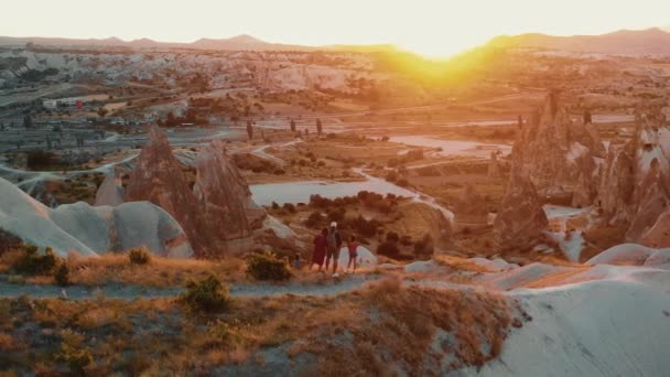 Drone vuela alrededor de la familia feliz con los niños viendo el panorama épico del amanecer en la cima de la roca de montaña en Capadocia. — Vídeo de stock