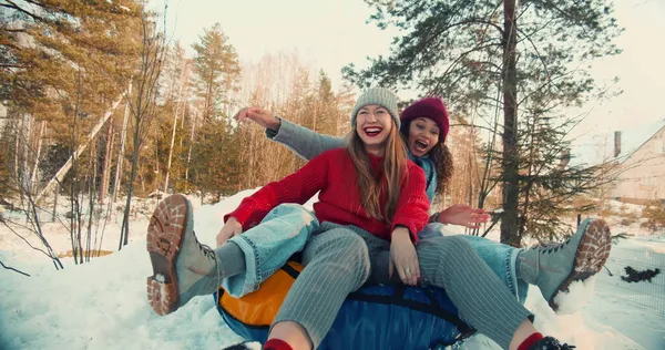 Dos amigos felices emocionados multiétnicos hermosas mujeres sonríen trineo en la pendiente de la nieve a la cámara, diversión de invierno cámara lenta. — Foto de Stock