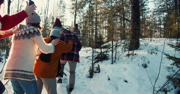 Camera segue felici amici multietnici a piedi sul soleggiato sentiero forestale invernale innevato il fine settimana di Natale escursione al rallentatore. — Foto Stock