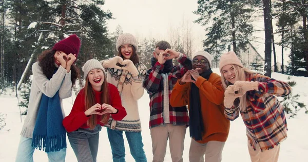 Grupo de amigos multiétnicos divertidos felices miran la cámara posando juntos, mostrando el gesto de amor en el bosque nevado cámara lenta. — Foto de Stock