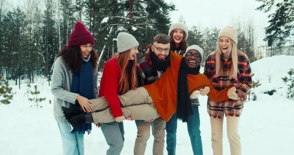 Зимові канікули. Щасливі багатонаціональні друзі, хитаючи африканського чоловіка, сміються разом у снігових лісах.. — стокове фото