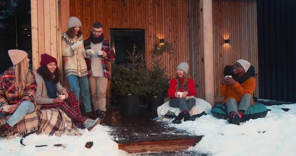 Nytårsferie ferie. Gruppe af glade venner drikker te taler på hyggelig juletræshus terrasse slow motion. Royaltyfrie stock-fotos