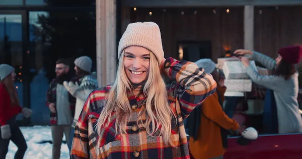 Wanita cantik berambut pirang muda yang gembira dengan topi musim dingin tersenyum pada kamera di pesta Natal teman-teman gerakan lambat. Stok Lukisan  