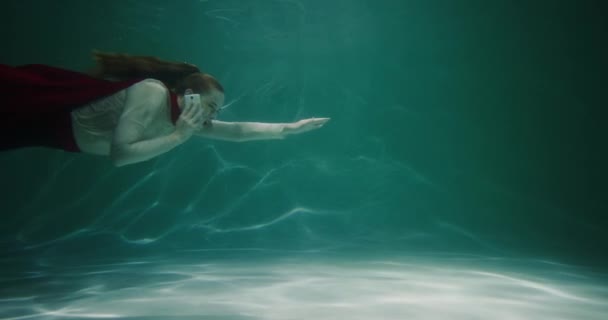 Концепция поддержки клиентов. Красивая молодая деловая женщина с плащом супергероя плавает под водой разговаривая по телефону замедленной съемки — стоковое видео