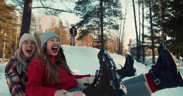 Vacaciones de invierno divertido. Dos hermosas mujeres felices emocionadas sonríen tirando en trineo en la pendiente del bosque de nieve hacia cámara lenta. — Foto de Stock