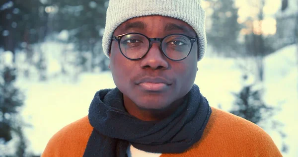 Close-up retrato de jovem homem africano feliz em roupas de inverno sorrindo, acenando para a câmera na floresta nevada câmera lenta. — Fotografia de Stock