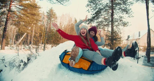 Deux multiethniques excités heureux beaux amis femmes sourire traîneau sur la pente de la neige à la caméra, plaisir d'hiver au ralenti. Images De Stock Libres De Droits