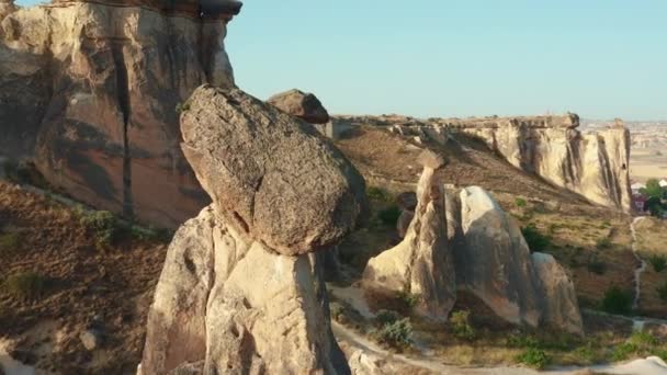 Dron latający w pobliżu pięknych tajemniczych wysokich skał z dużymi kamieniami na szczycie w pobliżu małego miasteczka w Cappadocia Turcja. — Wideo stockowe