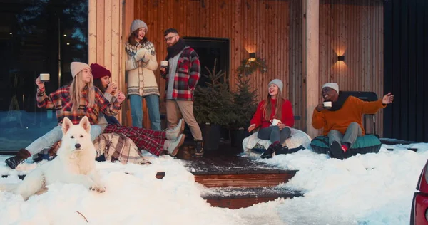 Веселая рождественская вечеринка. Группа счастливых друзей с горячими напитками танцуют в уютном зимнем домике замедленной съемки. — стоковое фото