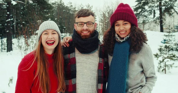 Glædelig jul. Glade multietniske unge venner poserer, smilende foran kameraet sammen på snedækket skov slow motion Royaltyfrie stock-fotos