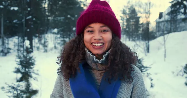 Temporada de invierno. Hermosa feliz emocionada estudiante de raza mixta mujer sonriendo a la cámara posando en el bosque nevado cámara lenta. Fotos de stock libres de derechos