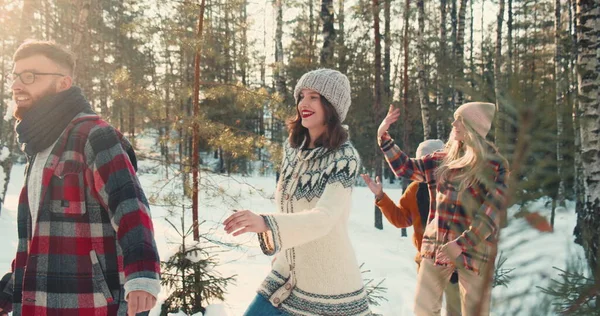 Genieten van de wintervakantie. Happy fun diverse vrienden lopen langs prachtige diepe sneeuw bospad samen slow motion. Stockfoto