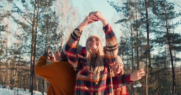 Camera beweegt rond gelukkig multi-etnische vrienden, elk neemt individuele selfie foto op zonnige winter bos slow motion. Rechtenvrije Stockafbeeldingen