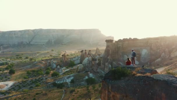 O drone voa pelo casal feliz que aprecia a vista épica do panorama da natureza do nascer do sol da rocha grande. Wanderlust e conceito de inspiração — Vídeo de Stock