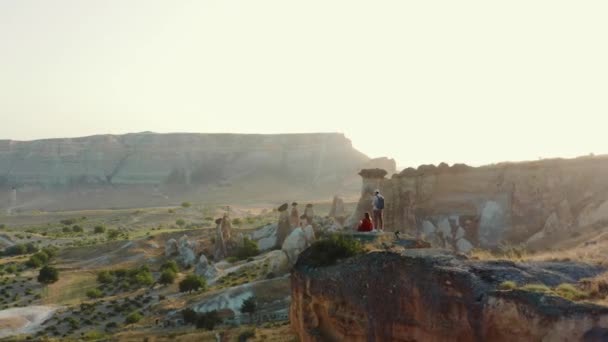 FREIHEIT UND REISE Überführung aus der Luft, glückliche Männer und Frauen beobachten majestätisches Sonnenaufgang Wüstenhimmelpanorama auf einem großen Felsen. — Stockvideo