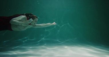 İnanılmaz sinematik ağır çekim, kırmızı süper kahraman pelerinli genç iş kadını ağır çekimde su altında yüzüyor..