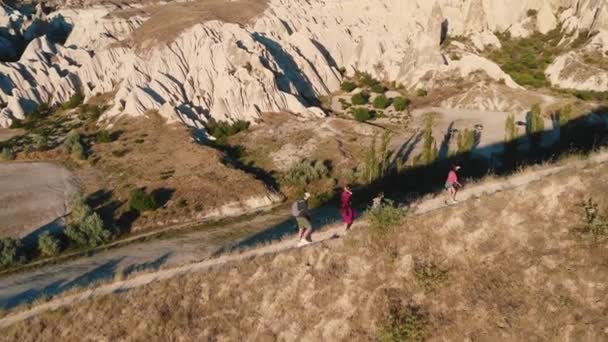 Drone suivi famille heureuse avec des enfants marchant le long du chemin jusqu'à la montagne lever du soleil profiter de la vue panoramique sur la Cappadoce. — Video
