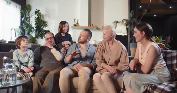 快乐快乐的祖父母、父母、少年男女在家里客厅的大沙发上聊天. — 图库视频影像