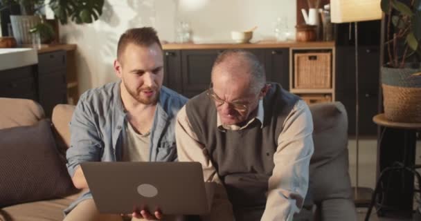 Ayudar a las personas mayores a utilizar la tecnología moderna. Feliz joven adulto enseñando a papá mayor de 70 años a usar la computadora portátil en casa. — Vídeos de Stock